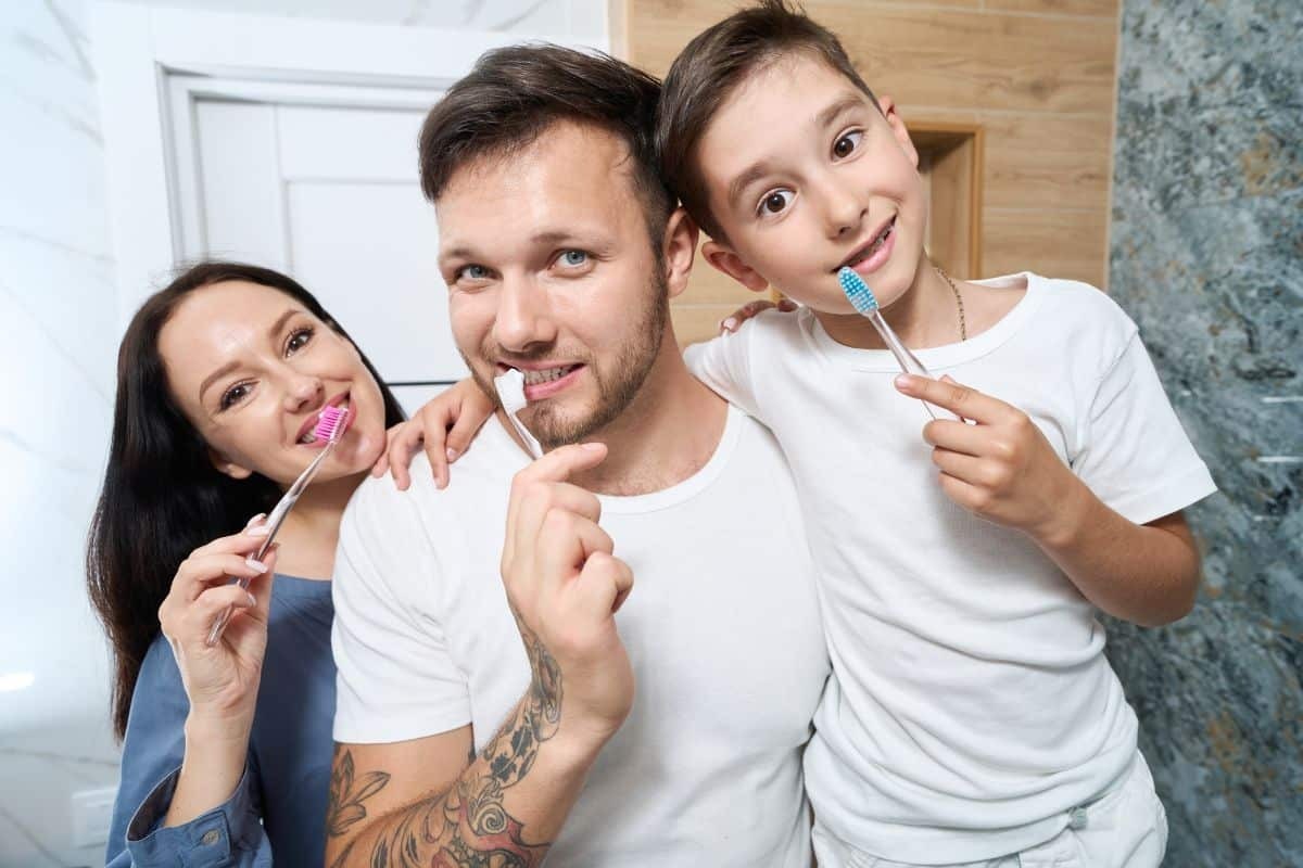 Happy family of three brushing teeth together in a bathroom.