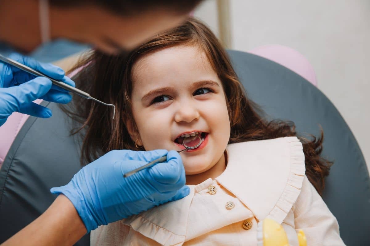 Young girl smiling during dental examination with dentist using tools to check her teeth.