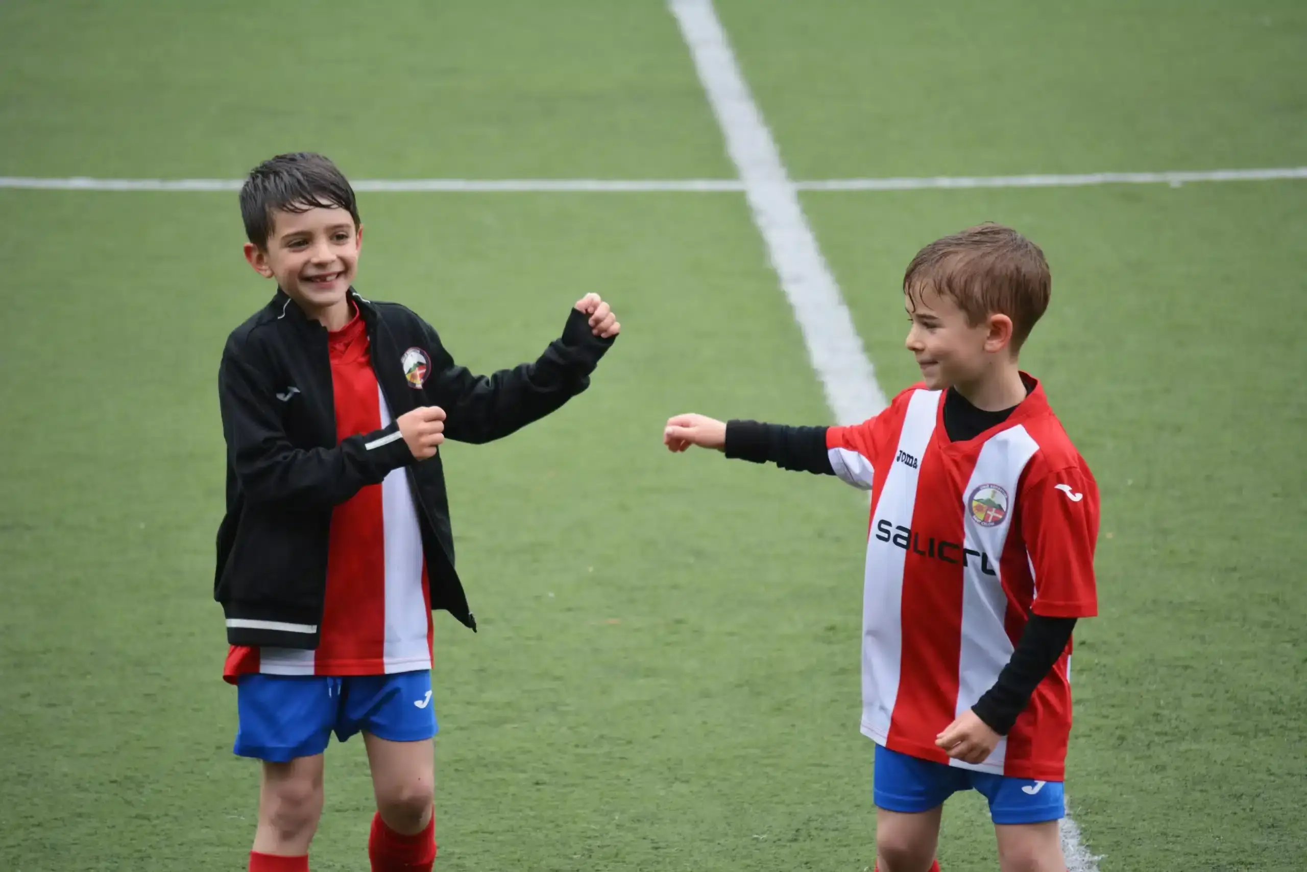 Two young soccer players in red and white uniforms smile together on field.