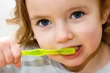 Young child brushing teeth with a green toothbrush and smiling.