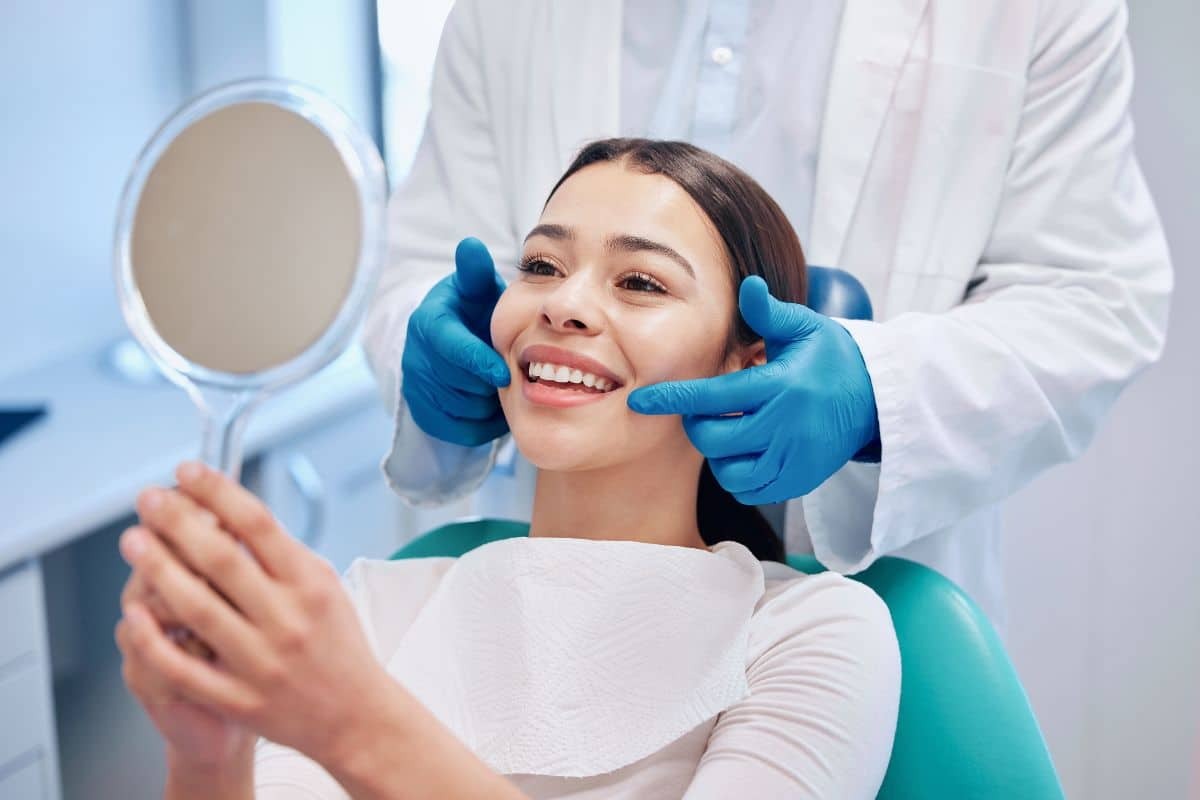 Smiling female patient viewing her teeth in mirror during dental examination with dentist in Albuquerque.