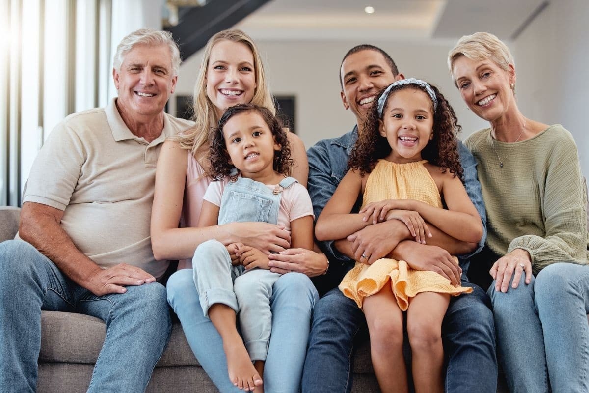 Happy multigenerational family smiling together on a couch during a dental checkup visit.